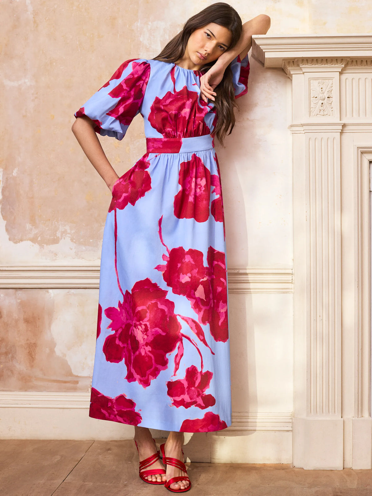 Woman wearing a floral dress against a beige wall.